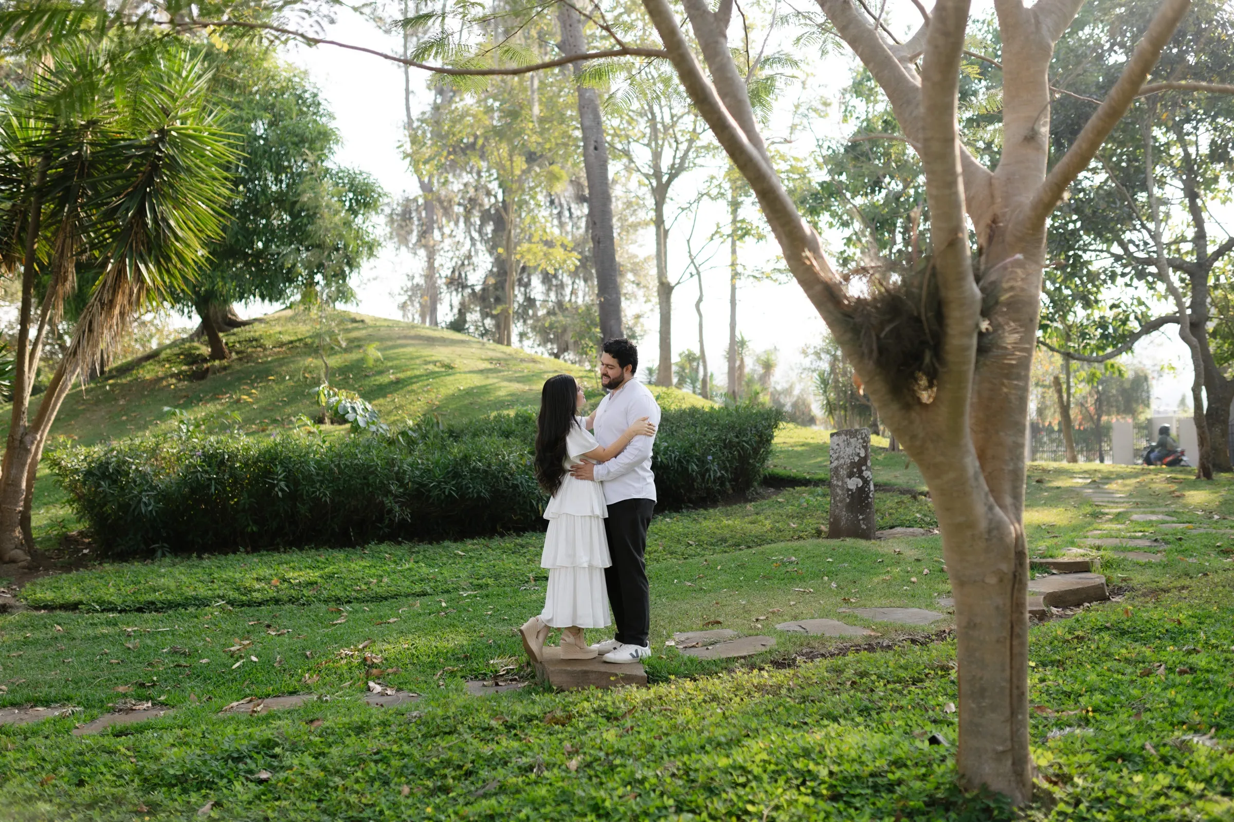 Josué y Katherine abrazados bajo los árboles de un jardín